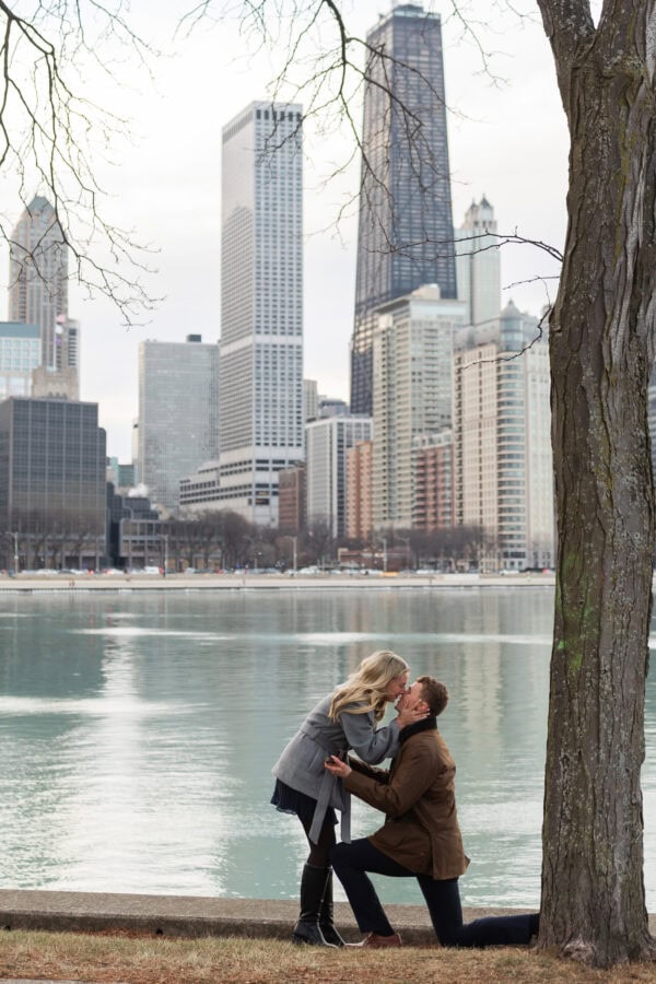 Man kneels to propose at Olive Park with Lake Michigan and Chicago's skyline in the background.