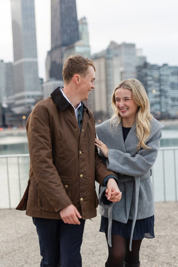 Happy engaged couple walks hand in hand along Chicago's lakefront during a winter engagement session.