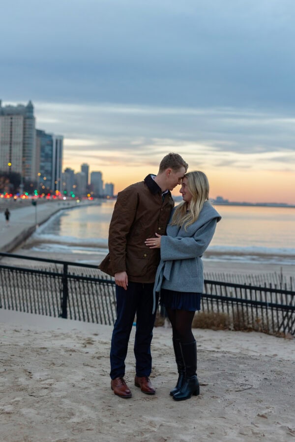 Couple stands on Chicago's lakefront beach at sunset after a surprise proposal and engagement