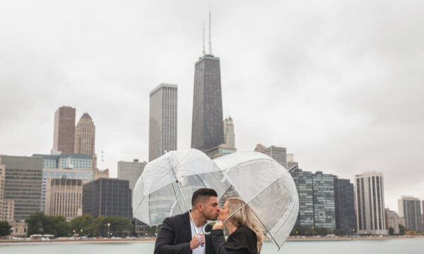 a couple holds umbrellas and share a kiss in front of the chicago skyline after getting engaged