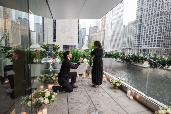 a man goes down on one knee as he proposes to his girlfriend on the terrace of RPM seafood on the chicago river.