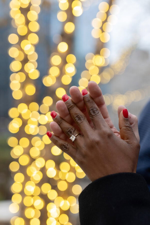 two hands are shown intertwined in front of glowing christmas lights.