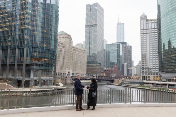 A couple stands in front of the Chicago River while the man does a card trick for his girlfriend