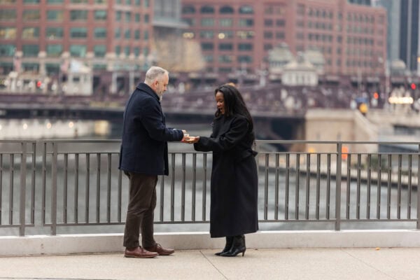 A couple stands in front of the Chicago River while the man does a card trick for his girlfriend