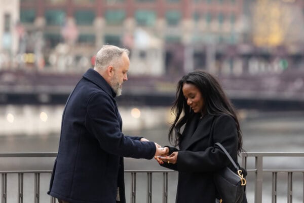 A couple stands in front of the Chicago River while the man does a card trick for his girlfriend