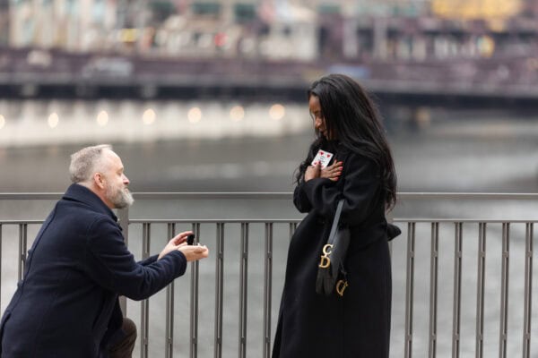 a man proposes to his girlfriend by using a card trick while they stand in front of the chicago downtown skyline at River Point Park