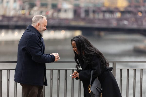 a man proposes to his girlfriend by using a card trick while they stand in front of the chicago downtown skyline at River Point Park