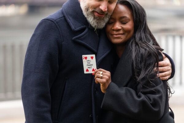 A newly engaged couple shows the card that says " will you marry me" that was used for their surprise Proposal