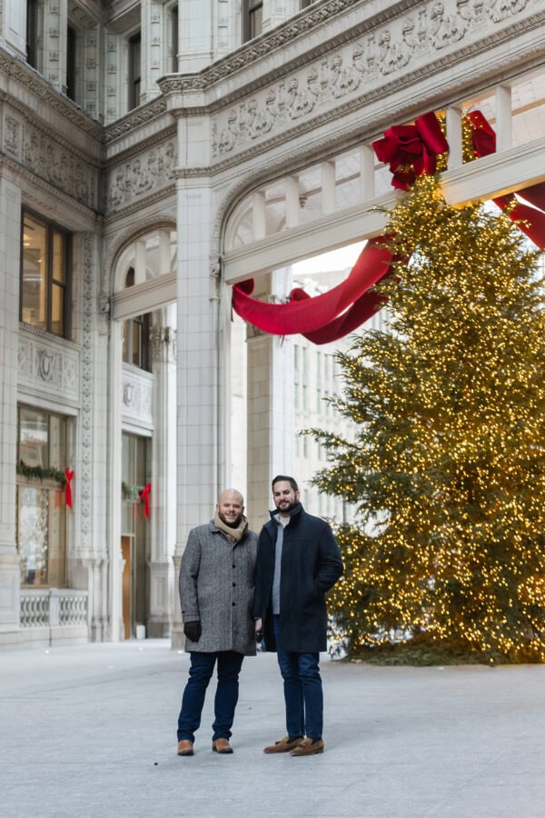 A same sex couple poses for an engagement photo at the Wrigley Building in Chicago with Christmas Tree